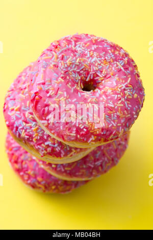 Rosa ciambella smerigliato con granelli colorati su sfondo giallo. Foto Stock