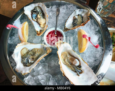 Un grande piatto di portata con ostriche delikatesnye su ghiaccio con calce servita con champagne e erbe aromatiche. Servire. Il telaio orizzontale. Foto Stock