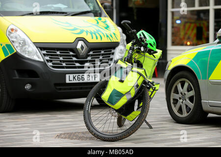 Medico di tre veicoli parcheggiati insieme, un ambulanza van, una bicicletta e un auto medica frequentare un emergenza in Kingston. Foto Stock