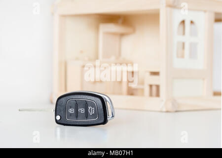 Chiavi auto con casa in legno modello in background. Scelta di byuing necessità di base. La decisione di priorità o di primaria necessità. Foto Stock