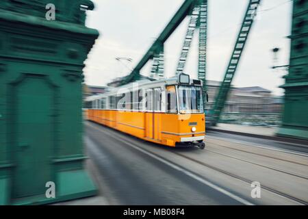 Il vecchio tram giallo in moto sul ponte in ferro. La vita della città di Budapest, Ungheria. Foto Stock