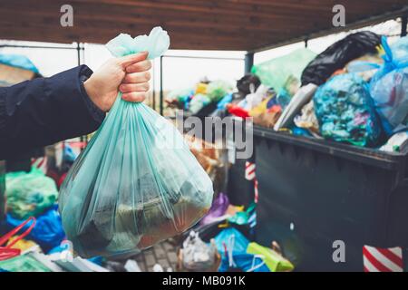 Mano con garbage contro il cestino pieno di lattine con sacchi per immondizia traboccare sul marciapiede. Foto Stock