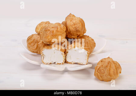 Profiteroles freschi bignè torte ripiene con crema pasticcera in un piatto bianco su bianco sullo sfondo di legno. popolare dessert Persiano Foto Stock