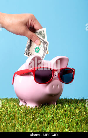 Mettere mano a un dollaro in una rosa salvadanaio indossando occhiali da sole. Foto Stock