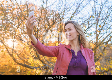 Pretty Woman tenendo selfie foto sul telefono cellulare in autunno park, Sud Australia Foto Stock