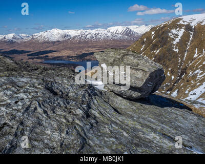 Una grande roccia seduto sul crinale che conduce alla vetta del Beinn Dorain nelle Highlands scozzesi con la Snow capped Blackmount colline nel backgro Foto Stock