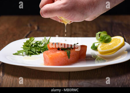 Versare il succo di limone su pezzi di salmone da limone crudo Foto Stock