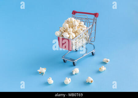 Carrello spesa toy pieno di popcorn pastello su sfondo blu la minima nozione. Foto Stock