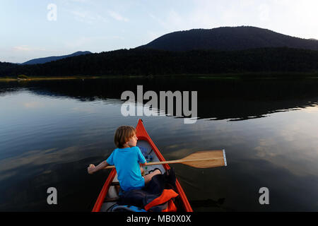 Ragazzo giovane paddling in una canoa su un lago al crepuscolo Foto Stock