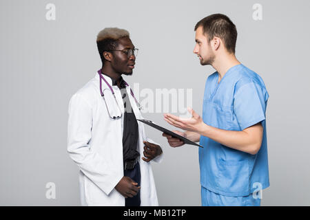 Due medici incontro e di consultarsi su sfondo grigio. Medico caucasica e afroamerican medico parlando abount pacient su grigio Foto Stock