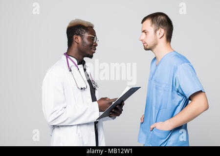 Due medici incontro e di consultarsi su sfondo grigio. Medico caucasica e afroamerican medico parlando abount pacient su grigio Foto Stock