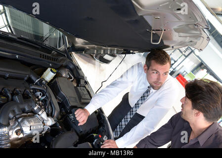 Venditori di auto e i clienti a parlare della tecnologia di un auto nello showroom di una concessionaria auto Foto Stock