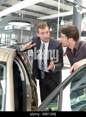 Venditori di auto e i clienti a parlare della tecnologia di un auto nello showroom di una concessionaria auto Foto Stock