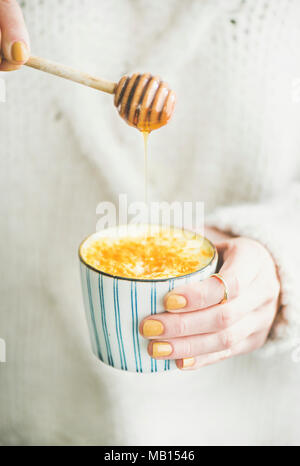 Vegano sano curcuma latte o latte dorato con miele nelle mani della donna che indossa un maglione bianco, close-up Foto Stock