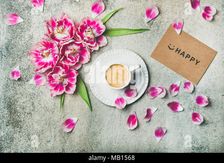 Mattina di primavera concetto. Flat-lay della tazza di caffè circondato con rosa tulip fiori e felice segno sulla carta al di sopra del marmo grigio Sfondo, vista dall'alto Foto Stock