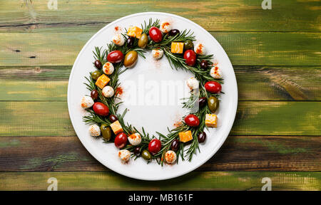 Il rosmarino ghirlanda di Natale antipasto con il formaggio e le olive su piastra su sfondo di legno Foto Stock