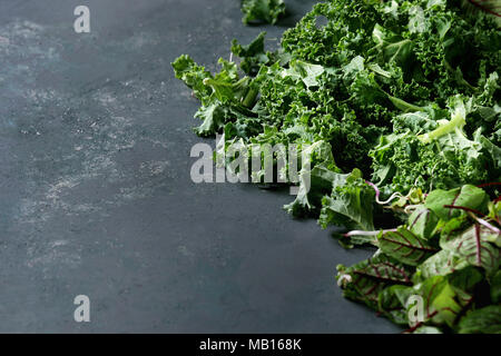 Insalata verde mix per insalata o smoothie con cavolo riccio, giovani foglie di bietola, germogli oltre il buio superficie texture. Copia dello spazio. Sfondo di cibo. Foto Stock