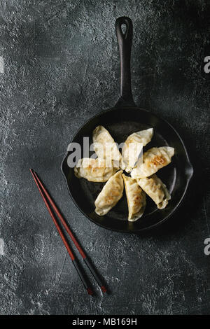 Asian Gyozas gnocco fritto potstickers su cast-padella di ferro, servita con bacchette nere su sfondo di texture. Vista superiore, spazio. Foto Stock