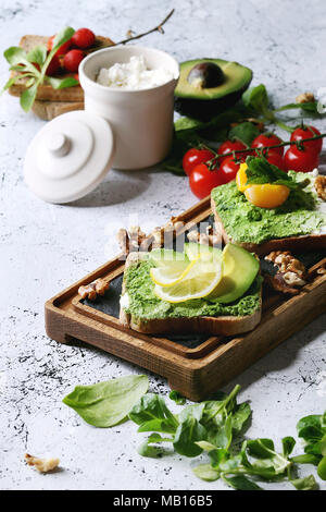 Sandwich vegetariano con avocado, ricotta, tuorlo d'uovo, spinaci, pomodori ciliegia sul grano intero pane tostato su legno scheda di ardesia con ingredienti abov Foto Stock