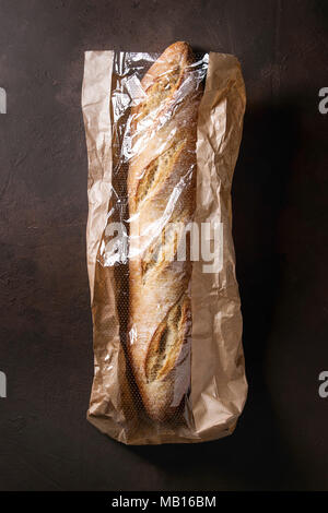 Filone di freschi di forno artigiano baguette di pane nel mercato sacchetto di carta su marrone scuro dello sfondo texture. Vista superiore, copia dello spazio. Foto Stock