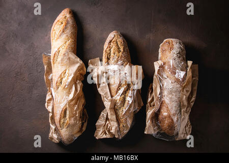 Varietà di polpettine di freschi di forno artigianale di segale, grano intero e il pane bianco in carta di mercato borsa in marrone scuro dello sfondo texture. Vista superiore, copia dello spazio. Foto Stock