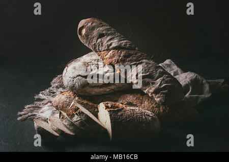 Varietà di polpettine sfornato fresco artigianale di segale e grano intero pane sulla tela di lino su marrone scuro dello sfondo texture. Copia dello spazio. Foto Stock