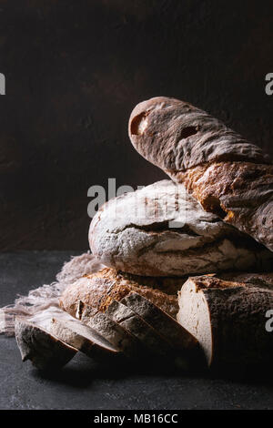 Varietà di polpettine sfornato fresco artigianale di segale e grano intero pane sulla tela di lino su marrone scuro dello sfondo texture. Copia dello spazio. Foto Stock