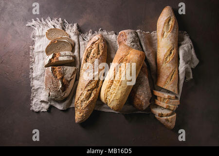 Varietà di polpettine sfornato fresco artigianale di segale, bianco e grano intero pane sulla tela di lino su marrone scuro dello sfondo texture. Vista superiore, copia dello spazio. Foto Stock