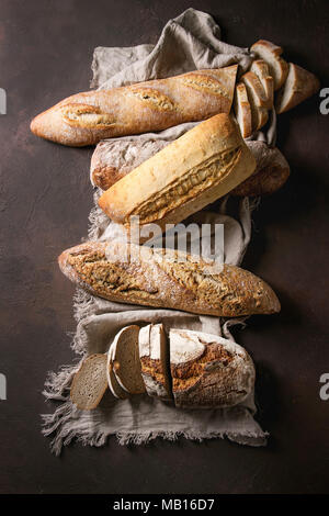 Varietà di polpettine sfornato fresco artigianale di segale, bianco e grano intero pane sulla tela di lino su marrone scuro dello sfondo texture. Vista superiore, copia dello spazio. Foto Stock