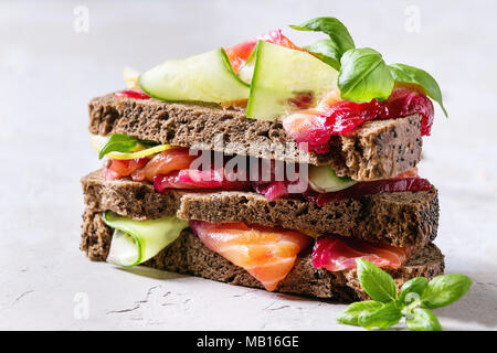 La barbabietola rossa a fette di salmone marinato panini con pane di segale, cetriolo, basilico e limone servita in pila sul tagliere di legno su grigio blu texture b Foto Stock