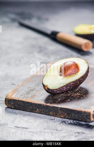 Verde avocado maturo f e il coltello su una pietra grigia sullo sfondo Foto Stock