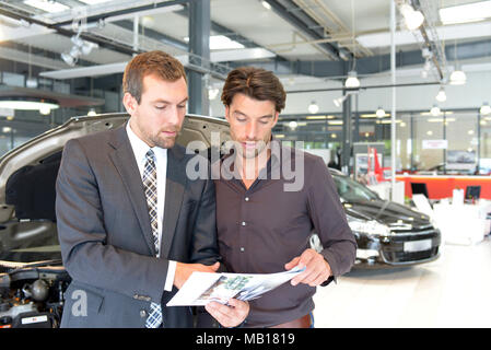 Venditori di auto e i clienti a parlare della tecnologia di un auto nello showroom di una concessionaria auto Foto Stock