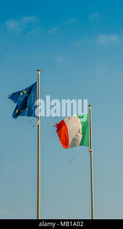 Bandiera dell'Italia ed Europa bandiera sventola insieme su un montante in isolato il cielo blu sullo sfondo. Concetto di trattamento finanziario, la moneta unica e il legame finanziario nonostante il lacerato i lati. Foto Stock