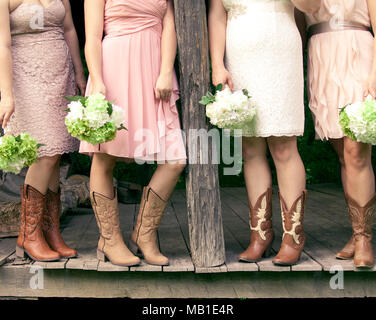 Quattro damigelle con mazzi di fiori e di indossare gli stivali da cowboy in un paese di nozze a tema Foto Stock