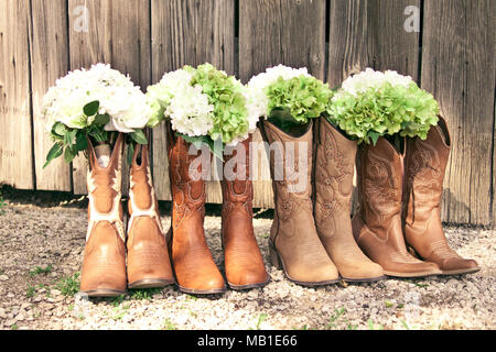 Stivali da cowboy e mazzi sono schierate dal grigio di un fienile in un paese di nozze a tema Foto Stock