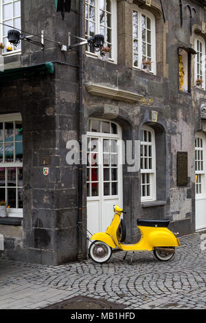 Un giallo vecchio modello scooter bloccata ad una tubazione di pioggia di una casa storica nel centro della città tedesca di Essen. Foto Stock