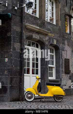 Un giallo vecchio modello scooter bloccata ad una tubazione di pioggia di una casa storica nel centro della città tedesca di Essen. Foto Stock