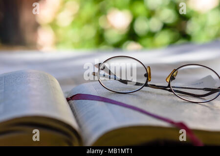 Vecchi occhiali bifocali giacciono sulla pagina biblica all aperto con camera per copiare il testo Foto Stock