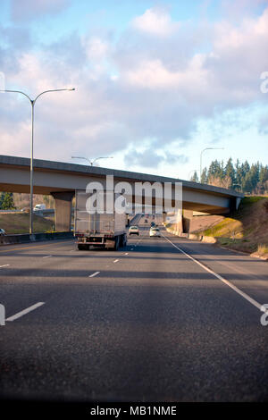 Big Rig semi carrello con dry van semi rimorchio passando sotto il ponte multiline divisa autostrada alla giornata soleggiata con nuvoloso cielo blu Foto Stock