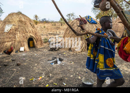 Omorate, Etiopia - Gennaio 24, 2018: una donna dalla tribù dei Mursi in posa per un ritratto vicino ad un albero con le tradizionali case dei Mursi in Etiopia Foto Stock