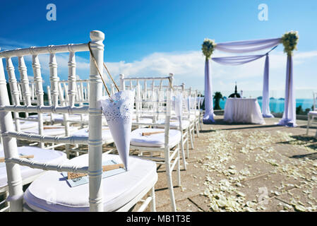 I matrimoni preparazione sulla collina, fiore minimo, la decorazione floreale per arco e altare, sedie bianche con cono di petali di rose con vista panoramica ocea Foto Stock