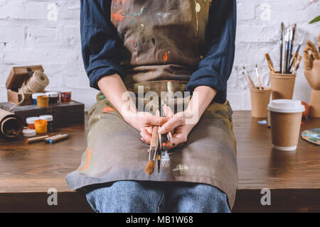 Immagine ritagliata della donna artista seduto sul tavolo e spazzole di contenimento Foto Stock