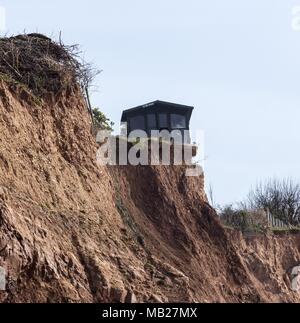 Sidmouth, 6th Apr 18. Un residente del Devon ha divertente mettere un avviso "for sale" sul suo capannone – come ora è arroccato pollici da una caduta di 100 piedi. Quattro cascate scogliera nella scorsa settimana hanno lasciato proprietà in Cliff Road, Sidmouth manca metri di giardino. La continua erosione di Pennington Point, ad est della città di Regency, ora mette in pericolo la foce del fiume Sid stesso, che se colpito potrebbe inondare una grande area della città. I costi di riparazione sono stimati a £72 milionse l'alluvione si è verificata. Foto Stock