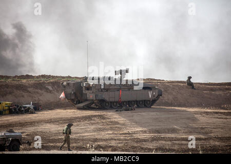 Jabalia, nel nord della Striscia di Gaza, 06 aprile 2018. Nirim, Israele. 06 apr, 2018. Un soldato israeliano guarda al suo cellulare come egli si trova accanto ad un veicolo militare come il fumo sale dalla combustione di pneumatici durante gli scontri tra forze israeliane e palestinesi lungo il confine Israeli-Gaza vicino Nirim, Israele, 06 aprile 2018. Credito: dpa picture alliance/Alamy Live News Foto Stock