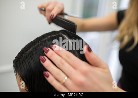 Ritagliato ritratto di parrucchiere mani di pettinatura dei capelli del cliente Foto Stock
