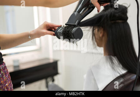 Ritagliato ritratto di parrucchiere per lo styling dei capelli del cliente con una spazzola ed essiccatore Foto Stock