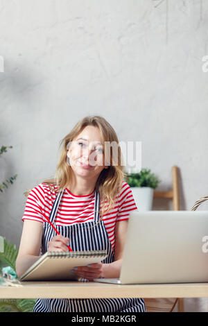 Ritratto di donna di fiorista con notebook a tavola con portatile su sfondo di fiori per interni Foto Stock