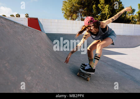 Femmina Skater corse su skateboard a skate park rampa. Giovane donna praticare lo skateboard all'aperto a skate park. Foto Stock