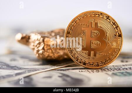 Golden bitcoin come principale world cryptocurrency accanto a grumo di oro con sfocato centinaia di dollari in banconote in background. Virtual digital web denaro blockchain valuta finanziare l'innovazione di business banking Foto Stock