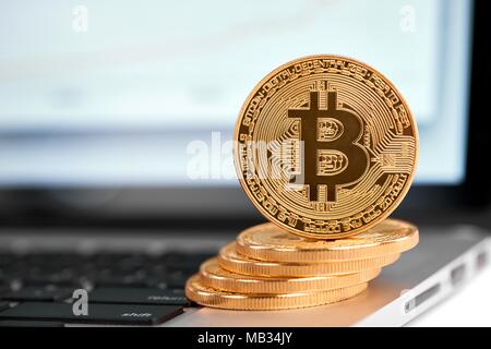 Pila di golden bitcoins con uno bitcoin sul suo bordo in piedi sul laptop di argento. Cryptocurrency virtual denaro digitale web moneta elettronica blockchain tendenze future sfondo sfocato Foto Stock